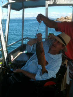 An accessible fishing boat with a man in a wheel chair holding up a fish he has caught.